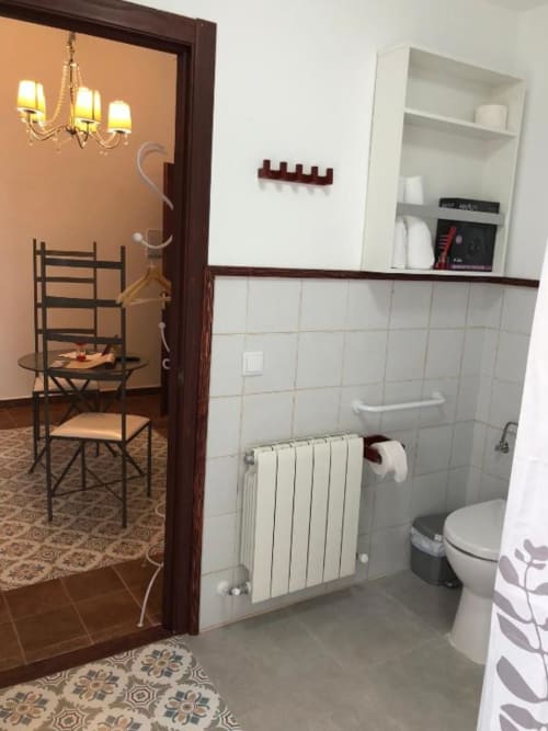Modern bathroom with white tile, radiator, toilet, and shelving at Retiro del Teatro hotel room in Ciudad Real, Spain