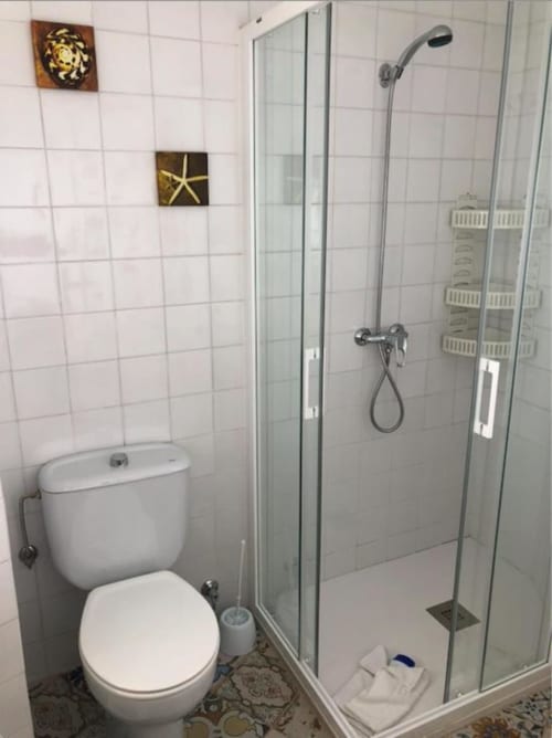 Baño moderno con paredes de azulejos blancos, inodoro y ducha con cabina de vidrio en la cabaña Villa Corral de Comedias del Complejo