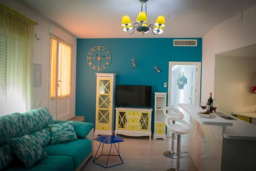 Sala de estar turquesa con muebles amarillos, sofá, mueble TV, comedor y araña en apartamento de Almagro