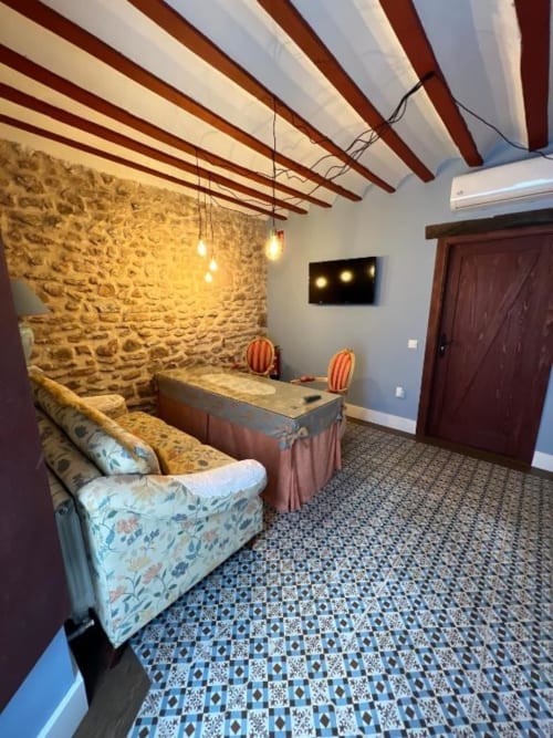Deluxe Suite with rustic stone wall, wooden beams, lounge seating, dining table, and modern amenities at Complejo Turístico