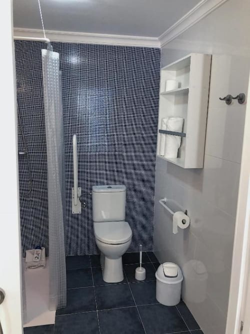 Modern bathroom with dark mosaic tile shower, white toilet, and accessible features in Deluxe Apartment at Complejo Turístico