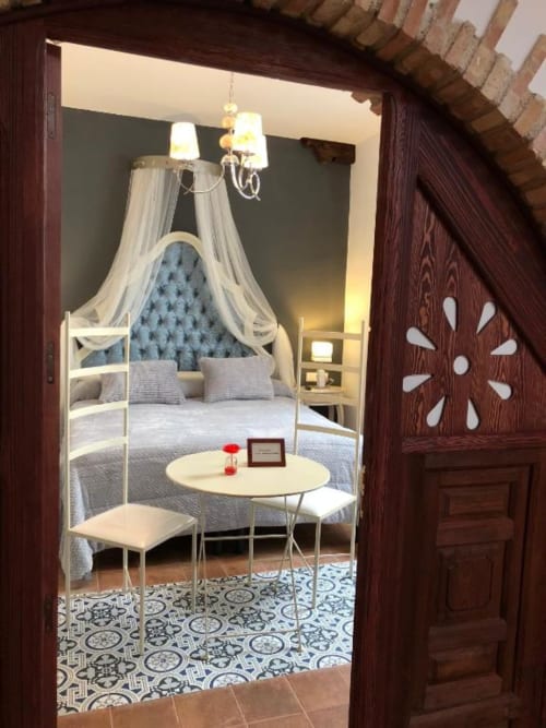 Elegant bedroom with canopy bed, blue tufted headboard, sheer curtains, and round table at Retiro del Teatro in Ciudad Real