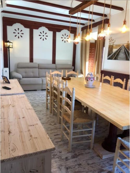 Espacioso apartamento de planta abierta con mesa de comedor de madera, sillas de asiento de junco, sofá gris, vigas expuestas e iluminación colgante
