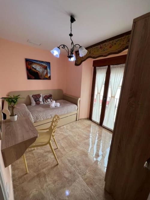 Dormitorio luminoso con cama diurna beige, lámpara de araña ornamental, paredes rosas, muebles de madera y puertas de vidrio en Retiro del Teatro