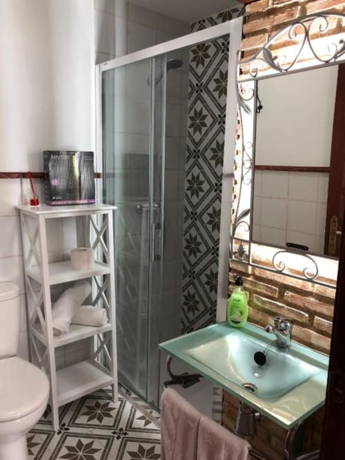 Modern bathroom with green sink, shower enclosure, mirror, white shelving, patterned tiles at Retiro del Teatro in Almagro.