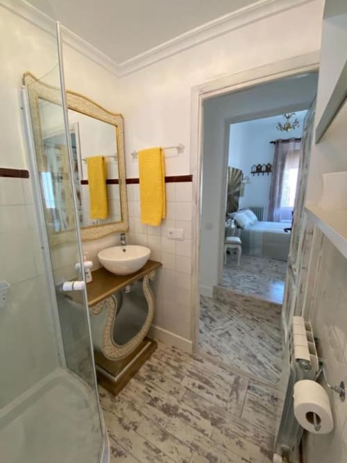 Baño moderno en la casita Villa Corral de Comedias con lavamanos redondo blanco, espejo marco dorado, toallas amarillas y acabado efecto madera