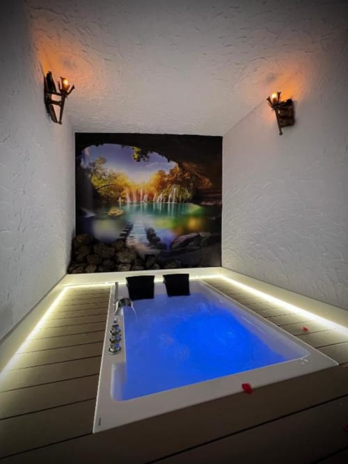 Luxury spa suite with illuminated jacuzzi, cave-view backdrop, wall sconces, and scenic waterfall landscape art at Complejo