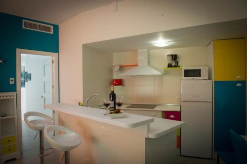 Cocina-comedor moderna en apartamento de Almagro con detalles coloridos, encimeras blancas, barra y acero inoxidable