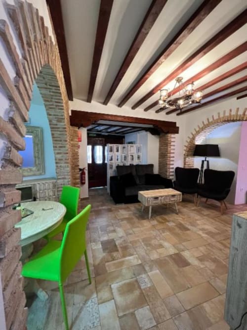 Modern apartment with exposed beam ceiling, brick walls, lime green dining chairs, black sofa, wooden table, and terracotta