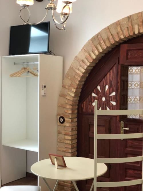 Hotel room with TV, white wardrobe, round table, and arched brick doorway in Almagro