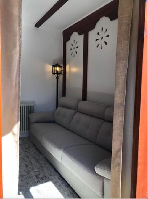 Sala de estar moderna con sofá gris, vigas de madera oscura, paneles decorativos e iluminación cálida en el Corral de Almagro