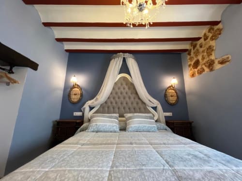 Luxury bedroom with canopy bed, blue accent wall, exposed beams, and elegant lighting in Almagro, Ciudad Real