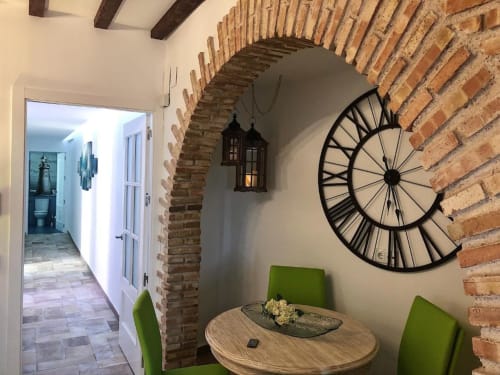 Rustic dining nook with brick arch, bicycle wheel decor, wooden table, and green chairs in Almagro hotel apartment