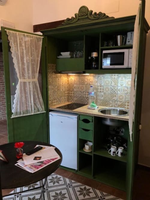 Green kitchenette with stove, microwave, refrigerator, and patterned tile backsplash in Almagro room at Complejo Turístico