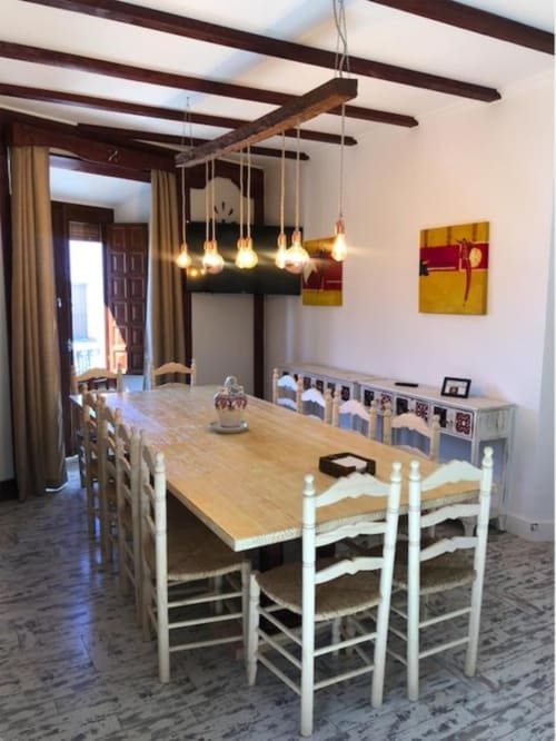 Comedor con mesa de madera, sillas blancas, vigas vistas, lámparas colgantes y obras de arte en el Apartamento Corral de Comedias,