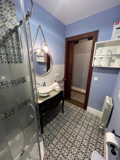 Modern bathroom with blue walls, patterned tiles, round mirror with light, sink, and shower at Complejo Turístico Retiro del