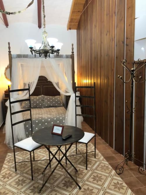 Elegant bedroom with four-poster canopy bed, sheer white drapes, chandelier, and round table in Almagro hotel room