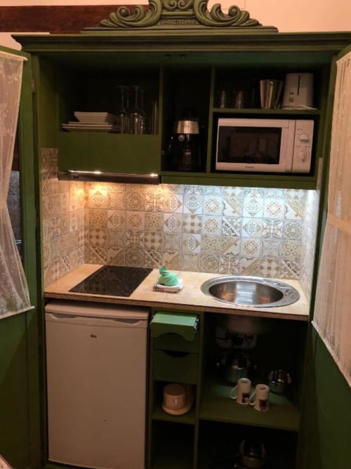 Compact kitchenette in green cabinet with microwave, sink, cooktop, refrigerator, and patterned tile backsplash at Complejo