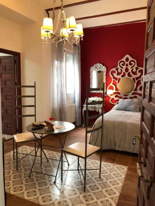 Romantic bedroom with red accent wall, decorative mirror, metal bed frame, round table, and ornate chandelier at Complejo