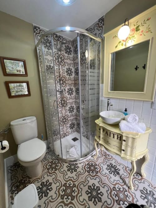 Deluxe Suite bathroom with decorative tile flooring, round shower enclosure, vessel sink, framed mirror, and cream vanity