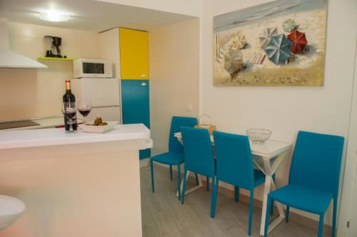 Moderna sala de estar y comedor con sillas azules, mesa blanca y armario amarillo en apartamento de lujo del complejo turístico