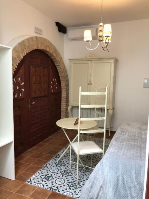 Rustic bedroom with arched wooden door, cream wardrobe, and white ladder chair at Retiro del Teatro, Almagro