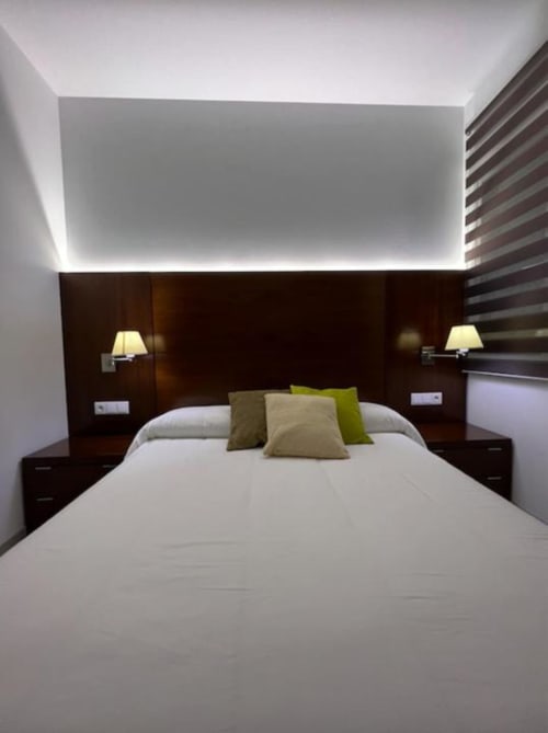Habitación moderna del hotel Almagro con sábanas blancas, cabecera de madera oscura, almohadas verdes e iluminación ambiental en el techo