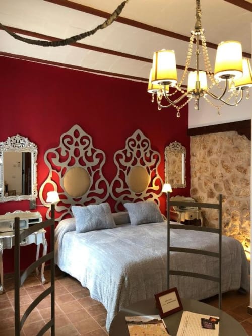 Dormitorio elegante con paredes rojas, espejos de cabecera blancos ornamentados, almohadas azules y lámpara de araña dorada en Complejo Turístico