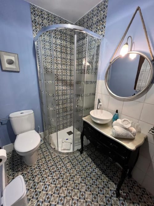 Modern bathroom with patterned tile flooring, walk-in shower, round mirror with rope detail, white sink and toilet in Double