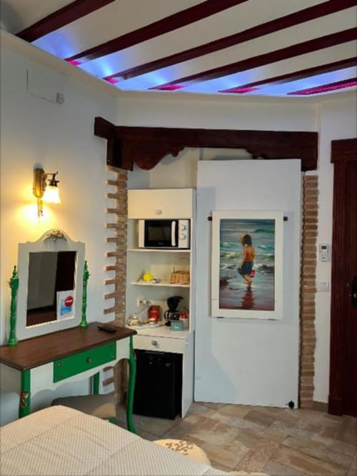 Modern suite with green accent furniture, kitchenette, microwave, beach artwork, LED ceiling, and brick columns in Almagro
