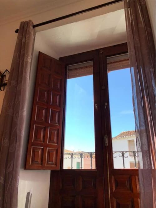 Puertas de madera abiertas con ventana transom con vistas a edificios históricos de Almagro y cielo azul despejado desde el Corral de Comedias