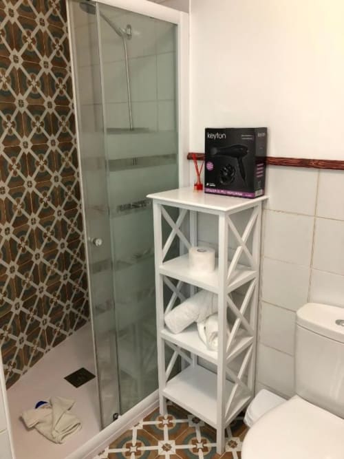 Modern bathroom with glass shower enclosure, white shelving unit with towels, and decorative patterned accents at Complejo