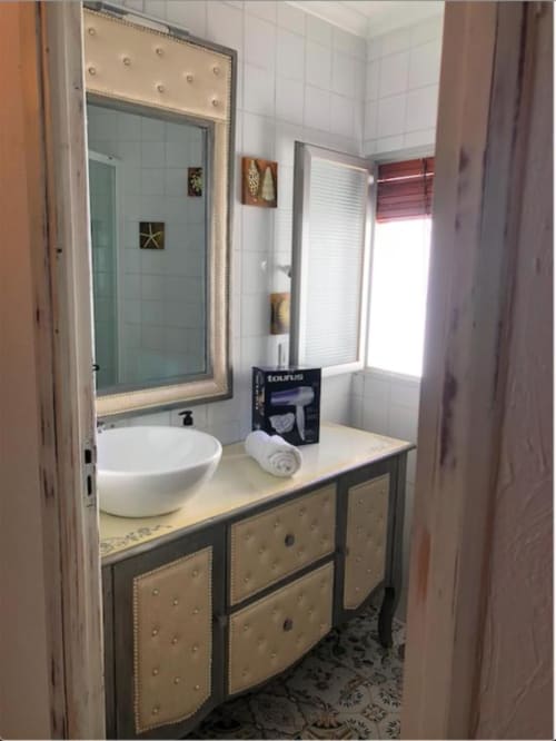 Baño moderno con lavabo redondo blanco, espejo enmarcado y mobiliario tapizado en beige del Apartamento Corral de Comedias