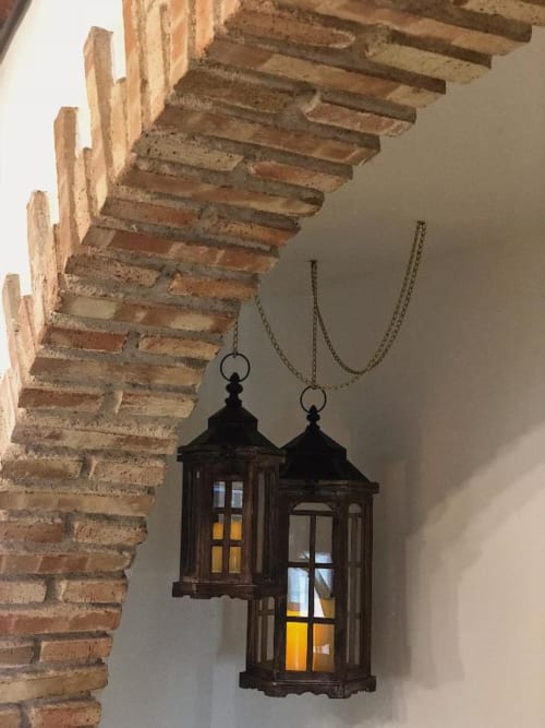 Two black decorative lanterns hanging from chains beneath exposed wooden beams in a historic cottage at Complejo Turístico