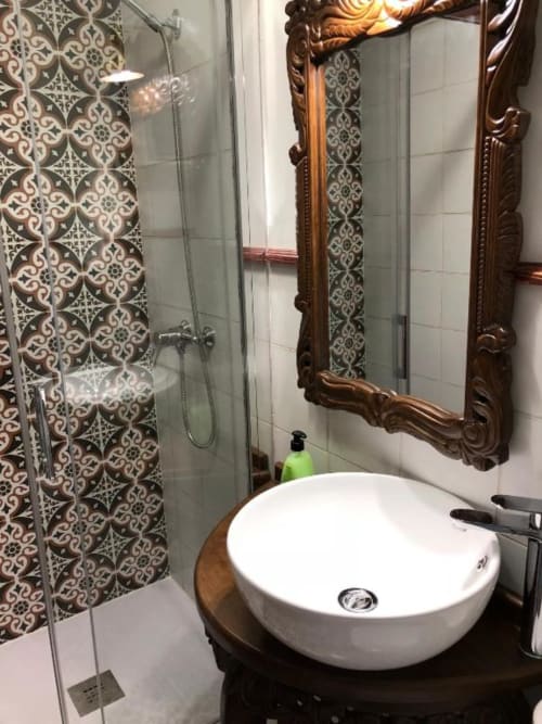 Modern bathroom with white round sink, ornate wooden mirror, patterned tile shower, and decorative wall tiles at Complejo