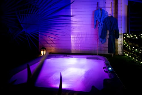 Luxurious purple-lit hot tub at Villa Eden Bleu, Biscarrosse, with tropical plants and elegant poolside ambiance at night