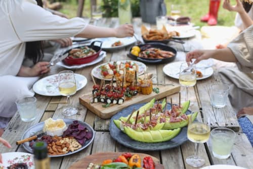 Réunion conviviale en jardín à La Ferme du Châtaignier avec élégants apéritifs, vin et plats colorés sur table en bois
