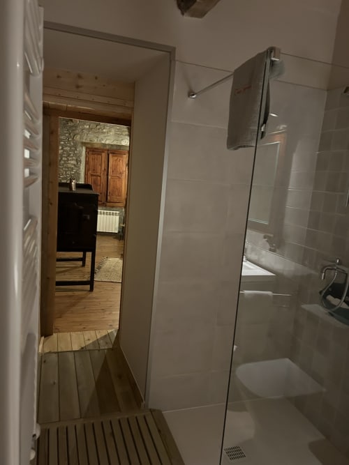 Cuarto de baño moderno con ducha de obra en la Casa Tapiolas, Molló. Mampara de cristal, azulejos, toallero y secador de pelo.