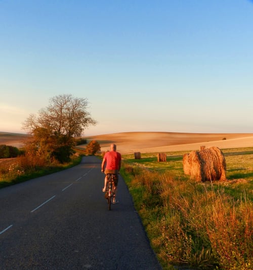 Radfahrer auf ländlicher Straße bei Pourrain mit Wellenfeldern und Heuballen zur goldenen Stunde