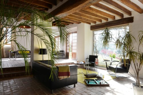 Élégant salon lumineux au Domaine de l'Ocrerie à Pourrain avec poutres bois, plantes et mobilier Bauhaus noir