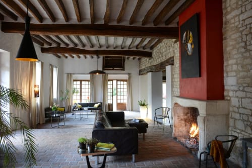 Le salon ouvert du Domaine de l'Ocrerie avec poutres apparentes, cheminée, mobilier noir et éclairage moderne à Pourrain
