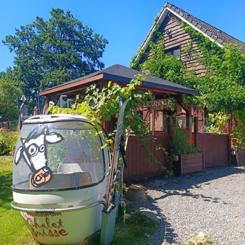 Vintage caravan met kunstwerken bij Les Refuges Du Chalet gastenverblijf in Jalhay, België, omgeven door klimop en groen
