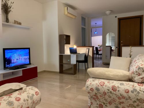 Moderno soggiorno a Treviso con divano floreale, TV, scrivania e vista città dalla grande finestra