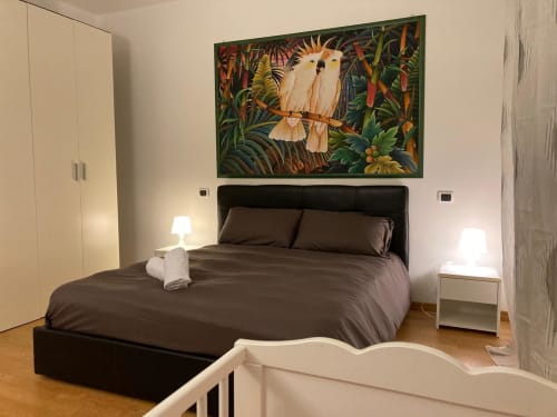 Camera moderna dell'Apartment GioviGemini a Treviso con letto nero, comodini bianchi e quadri di uccelli tropicali