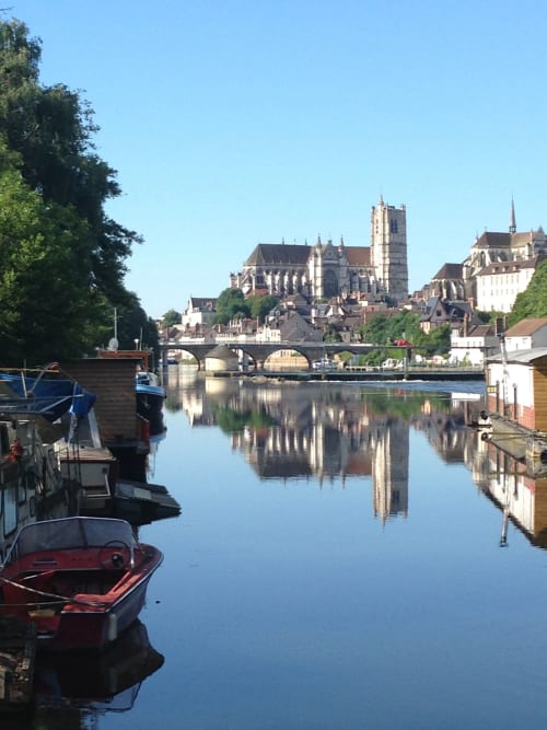 Scenic river view with historic cathedral, boats, and stone bridge in Pourrain, France
