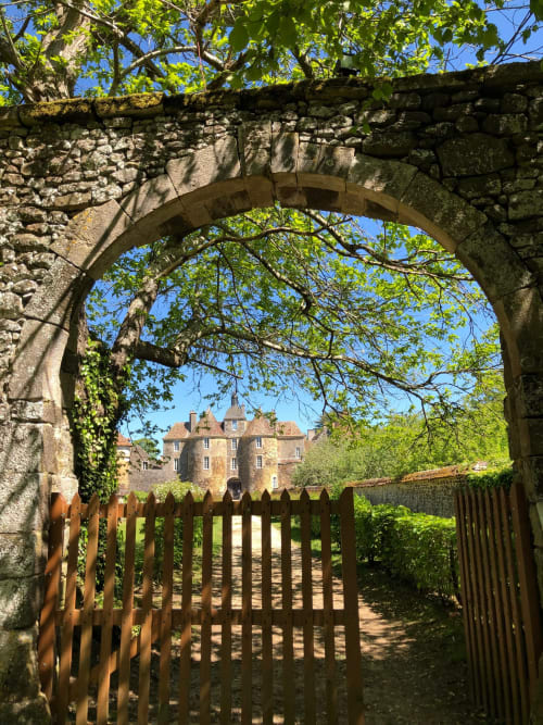 Stone archway with wooden gate framing medieval château at Domaine de l'Ocrerie, Pourrain, France