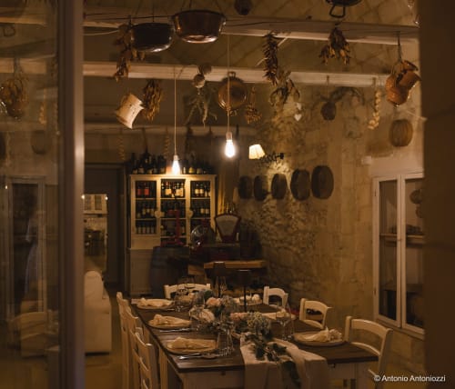 Sala da pranzo rustica presso la Masseria Vittoria con erbe aromatiche appese, luci a sospensione e tavolo preparato ad Acaya, Vernole