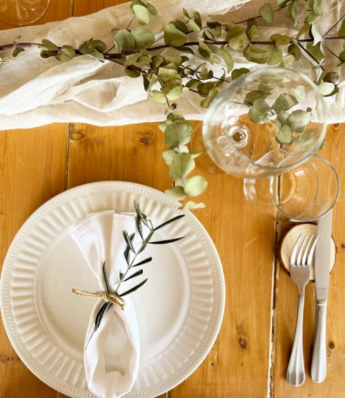 Elegante allestimento tavolo a Masseria Vittoria con piatti bianchi, ghirlanda di eucalipto e bicchieri su tavolo di legno ad Acaya