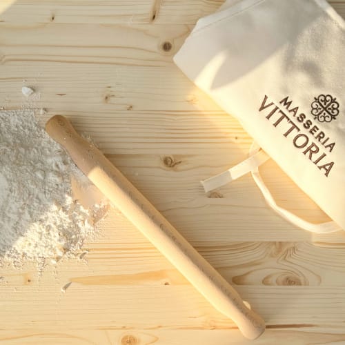 Preparazione della pasta presso la Masseria Vittoria con farina, mattarello e grembiule su superficie di legno