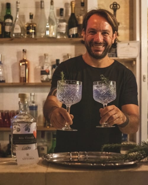 Barista sorridente alla Masseria Vittoria B&B di Acaya con due cocktail gin guarniti di rosmarino